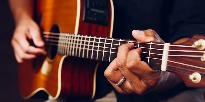 Nahaufnahme einer Hand, die auf einer Akustikgitarre mit Kapodaster einen Akkord greift
